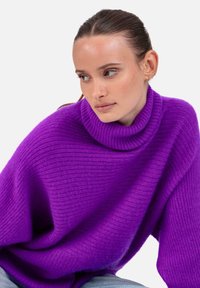 Pull à col roulé côtelé violet avec une coupe ample. Texture douce, encolure large et tombé décontracté. Associé à un jean bleu clair.