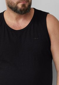 Schwarz ärmelloses Baumwolltanktop mit rundem Ausschnitt und subtilen Logodetails auf der Brust. Weiche Textur mit lockerer Passform.