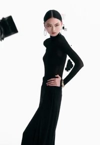 Svart langermet tettsittende høyhalset topp kombinert med et flytende svart skjørt. Modellen accessoriserer med hoopsmykker og et armbånd.