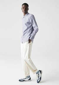 Button-down shirt in blue and white stripes, paired with cream-colored trousers and navy sneakers, featuring a casual fit and rolled cuffs.