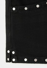 Tissu en denim noir avec des rivets en métal argenté le long du bord de la poche et des coutures, mettant en valeur les détails de couture texturés.