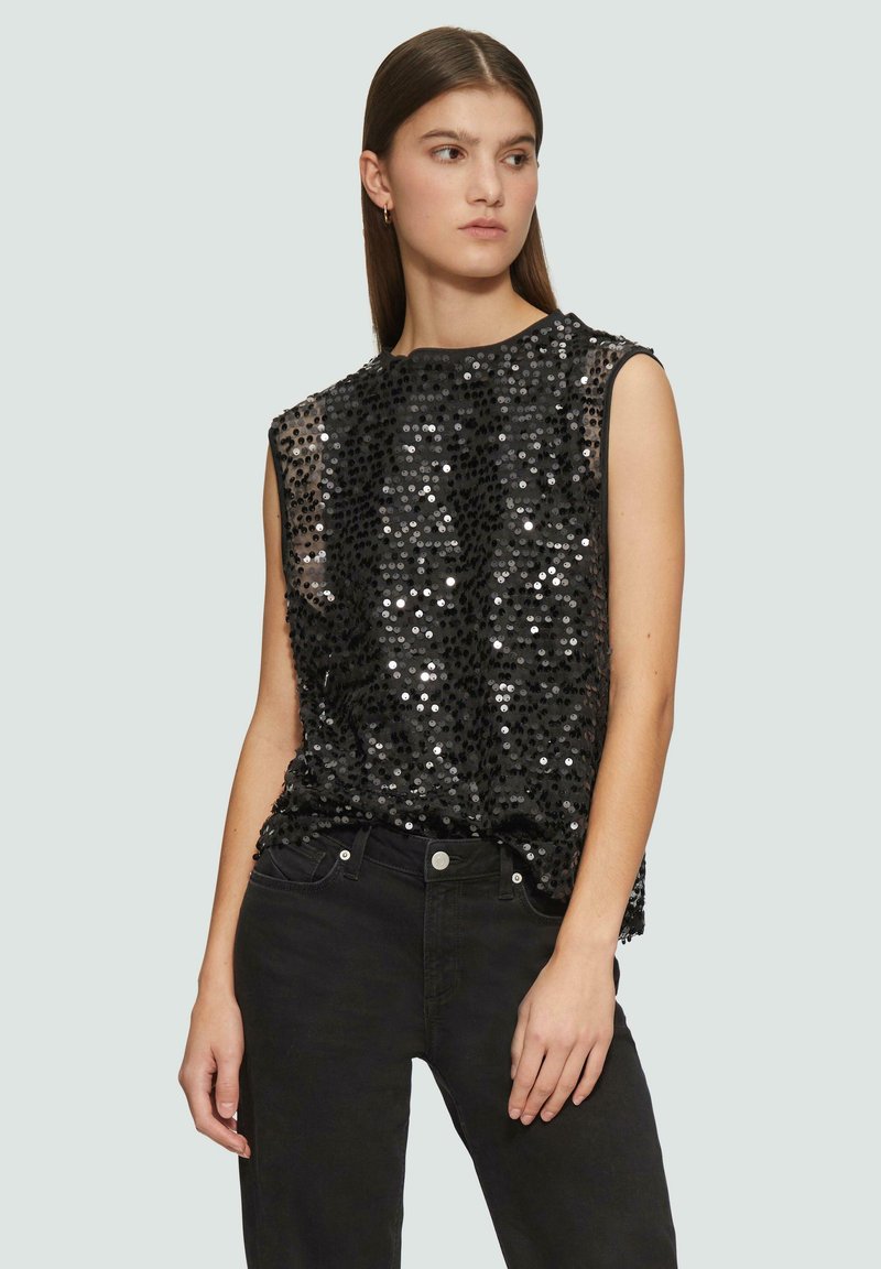 Schwarzes ärmelloses Top mit Pailletten und strukturiertem Oberflächenmaterial, rundem Ausschnitt und lockerer Passform. Kombiniert mit schwarzen Jeans.