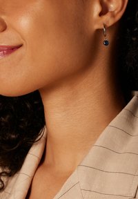 Boucle d'oreille en argent avec un pendentif en pierre précieuse bleue, surface lisse, forme ronde, portée à l'oreille, le modèle porte une tenue à rayures discrètes.