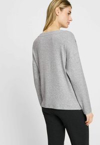 Grijze, gemêleerde trui met een relaxte pasvorm en brede halslijn, van achteren gezien, gecombineerd met donkere broek. Subtiel stikseldetail bij de schouders.