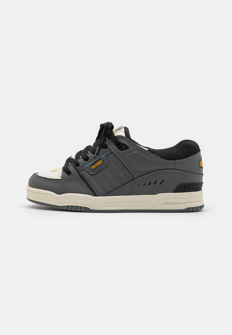 Gray sneaker with black accents and a textured surface. Features a cream outsole, black laces, and side ventilation holes. Brand logo visible.