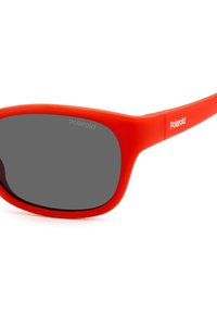 Occhiali da sole rossi in plastica con design curvato, lenti grigie e logo "Polaroid" sul lato. Trama liscia opaca e montatura robusta.