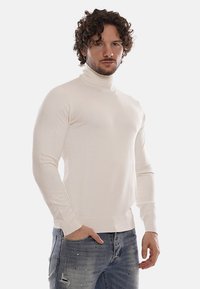 Maglione a collo alto di colore avorio, realizzato in morbido knit. Design aderente con maniche lunghe e polsini a coste, abbinato a jeans blu strappati.