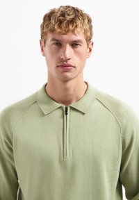 Lichtgroene pullover met een ritskraag, met raglanmouwen en een zachte textuur. Eenvoudig ontwerp zonder zichtbare patronen of accenten.