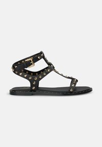 Sandali piatti neri con accenti dorati a borchie, caratterizzati da un design open-toe e una cinghia alla caviglia regolabile, realizzati in materiale sintetico.