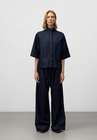 Completo in denim scuro composto da una maglietta a maniche corte con colletto e tasca, abbinata a pantaloni larghi, caratterizzati da un fit rilassato e una texture particolare.