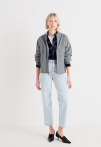 Veste bomber zippée grise sur une chemise à carreaux noire et bleue, assortie à un jean taille haute bleu clair et des escarpins noirs à bout pointu.