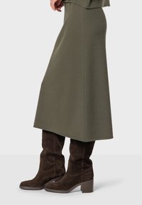 Gonna verde oliva realizzata in tessuto morbido, di forma A-line, abbinata a stivali al ginocchio in suede marrone scuro con tacco a blocco.