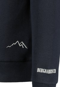 Marineblauwe sweatshirts met een bergafbeelding en "BERGNARRISCH" tekst in witte borduuring op de mouw. Zacht materiaal met geribde manchetten.