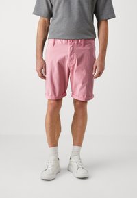 Lys rosa bomullsshorts med rullekanter, sidelommer og frontknapplukking. Brukt med en grå t-skjorte og hvite joggesko.