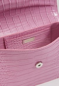 Interno di una borsa a mano in pelle rosa con effetto coccodrillo, caratterizzato da una texture morbida, una tasca e una chiusura a pressione in tonalità argento.