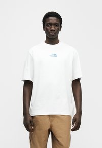 Λευκό βαμβακερό μπλουζάκι με κοντά μανίκια, με μπλε λογότυπο στο στήθος. Απλή, άνετη γραμμή και λεία υφή. Καθημερινό σχέδιο.