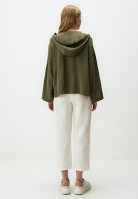 Felpa cropped verde oliva con un grande cappuccio e maniche larghe, abbinata a pantaloni bianchi a gamba larga e sneakers beige. Tessuto dal tocco morbido.