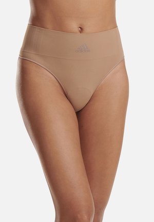 Mujer vistiendo ropa interior beige de cintura alta sin costuras de Adidas, mostrando el ajuste y el logo sobre un fondo neutro.