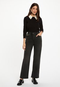 Suéter negro de canalé con un cuello blanco, que presenta detalles decorativos. Combinado con jeans negros de tiro alto y pernera ancha, y zapatos negros brillantes.