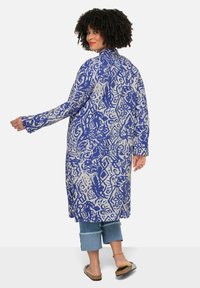 Lang, lichtgewicht jas met een blauw-wit abstract patroon, voorzien van een kraag en een open voorkant, gecombineerd met casual, cropped spijkerbroek.