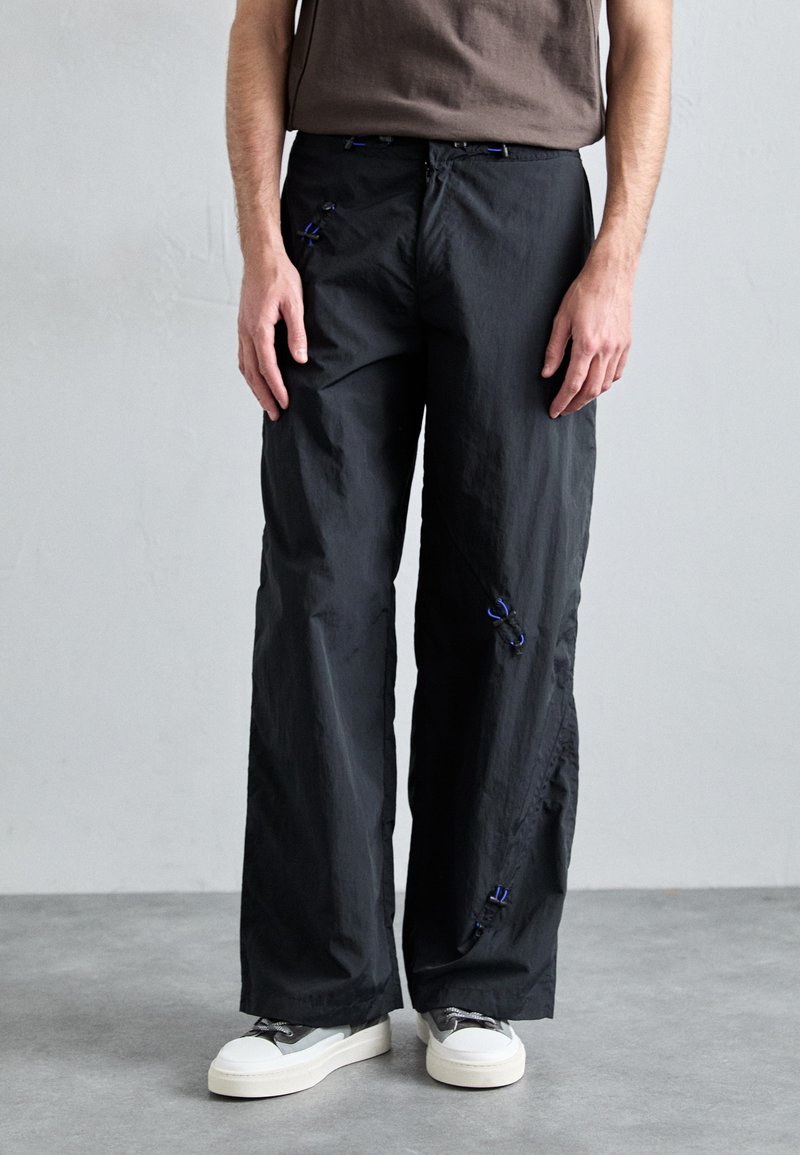 Black cargo pants with a loose fit, featuring blue accents, material texture with a slight sheen, and visible pockets with ties.