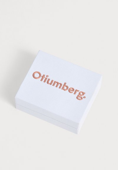 Λευκό ορθογώνιο κουτί με τη λέξη "Otiumberg" ανάγλυφη με μεταλλικά χρυσά γράμματα στο καπάκι, τοποθετημένο σε απλό, ανοιχτό φόντο.