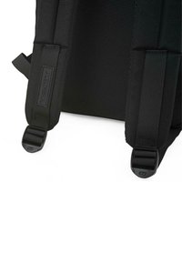 Mochila negra con correas de webbing ajustables, hebillas seguras y una construcción de tela texturizada. Acento del logo en la correa.