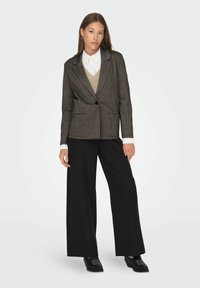 Brown plaid blazer with a single button, paired with a beige sweater vest and white shirt, complemented by wide-leg black pants and black shoes.