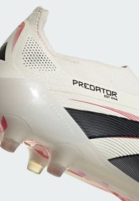 Vit idrottssko med svarta ränder och röda accenter. Har en strukturerad ovandel, halvtransparent sula och lågskuren design.