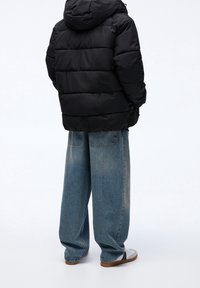 Giubbotto imbottito nero con cappuccio, caratterizzato da cuciture orizzontali. Abbinato a jeans in denim chiari e larghi di colore blu e sandali con suola marrone.