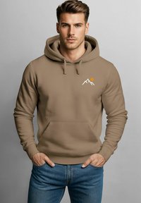 Braun Kapuzenpullover mit Fronttasche, versehen mit weißen Bergen und Grafiken einer orangefarbenen Sonne. Weicher Stoff, Kordelzugkapuze und gerippte Bündchen.