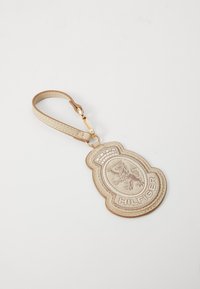 Chaveiro de couro bege com logotipo de leão em relevo e texto "HILFIGER". Possui uma alça plana com hardware dourado e costuras visíveis.