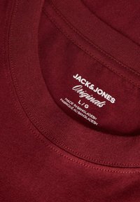 Burgundia puuvillane T-särk ümmarguse kaelusega, millel on valged trükitud sildid Jack & Jones ja valmistatud Bangladeshs.
