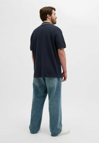 Dunkelblaues Polohemd für Herren mit kurzen Ärmeln, kombiniert mit lockeren, hellblauen Jeans. Tagloses Design, lässiger Stil und aus Baumwolle gefertigt.