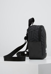 Svart axelremsväska med geometrisk textur. Har dragkedja, justerbar rem och en logotyp detalj på framsidan. Kompakt och rektangulär form.