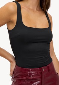 Zwarte mouwloze bodysuit met een vierkante halslijn, met een gladde textuur. Gecombineerd met een hoog uitgesneden bordeauxkleurige nepleerrok met krokodilstructuur.