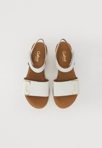 White leather sandals with a wide strap, gold-tone buckle detail, tan footbed, and an open back design for easy wear.