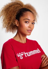 Rød bomulds T-shirt med et fremtrædende hvidt "hummel"-logo og et bi-ikon. Rund hals, korte ærmer, glat tekstur.