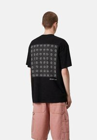 Camiseta negra de manga corta con un diseño de cuadrícula de patrones en blanco de calaveras y corazones en la parte posterior; material de algodón, corte relajado.
