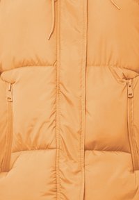 Pufferjack in zacht oranje materiaal, met een hoge kraag, twee zijzakken met ritssluitingen en gestikte panelen voor extra isolatie.