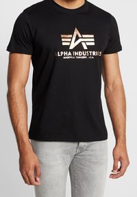 Zwarte katoenen t-shirt met een metallic rosegouden logo, geometrische elementen en tekst, korte mouwen en een ronde hals.