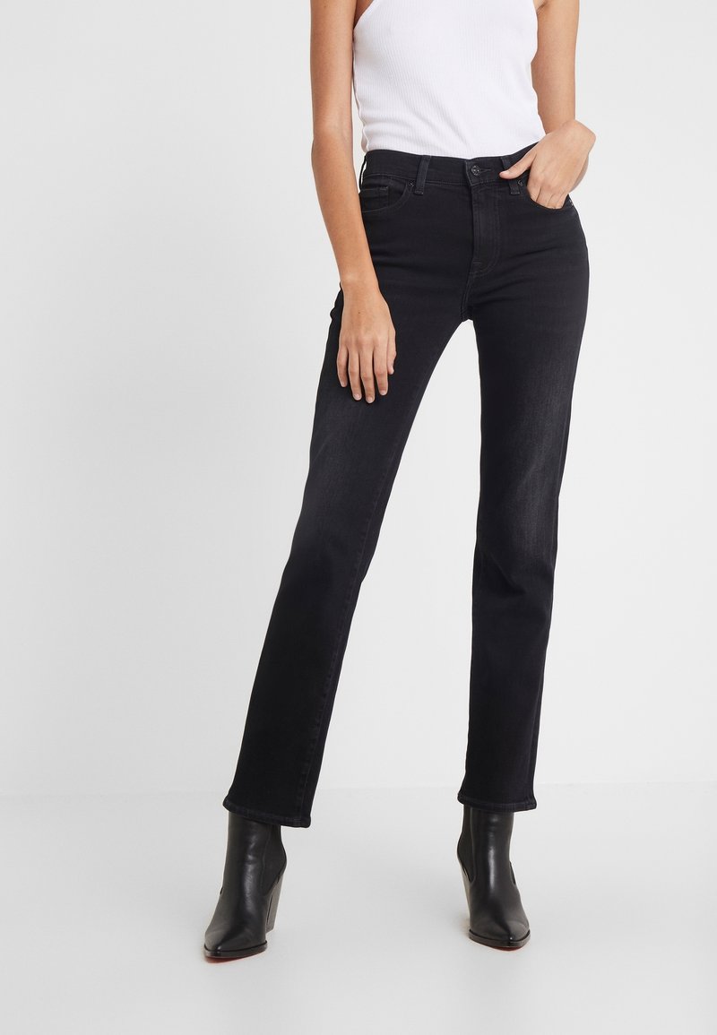 Jeans negros con corte recto, que presentan un diseño clásico de cinco bolsillos y un ligero estiramiento para mayor comodidad. Llevados con botas de tacón negras.