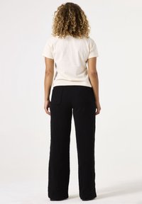 Camiseta corta de manga corta en color crema combinada con pantalones de pierna ancha texturizados en negro, con dos bolsillos traseros, mostrada desde la parte de atrás sobre un fondo neutro.