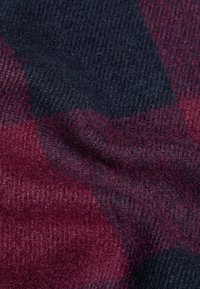 Tessuto morbido piegato con vista ravvicinata che mostra un motivo a quadri texturizzato in blu scuro e bordeaux.