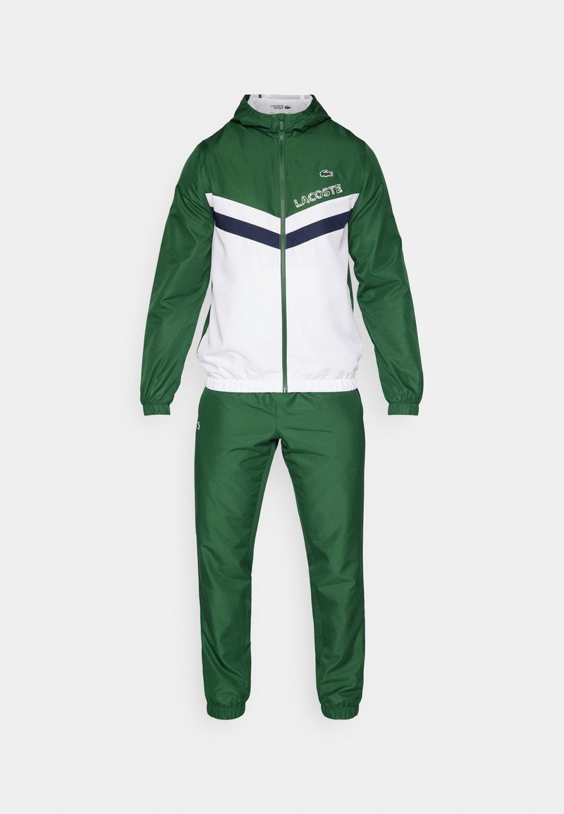 Tuta sportivo zip-up verde e bianco con cappuccio, caratterizzato da un design a chevron blu navy sulla giacca, con polsini e vita elasticizzati, realizzato in materiale leggero.