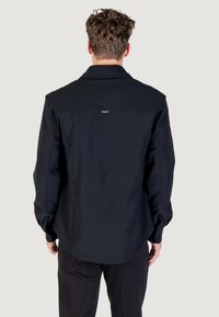 Crna softshell jakna s ovratnikom, dugim rukavima i suptilnim logotipom na leđima. Glatka tekstura i kroj koji prati liniju tijela.