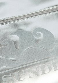 Busta metallizzata argentea con una superficie liscia, presenta motivi in rilievo di sole e onde, e una chiusura a zip lungo la parte superiore.