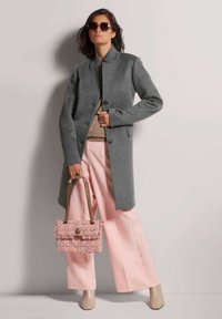 Grijs wollen mantel met hoge kraag, knoopsluiting, gecombineerd met een beige trui, roze wijde broek en een gestructureerde roze handtas.