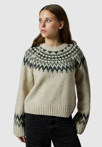 Beżowy sweter wełniany z okrągłym dekoltem, zdobiony ciemnozielonymi wzorami geometrycznymi wokół karczku oraz prążkowanymi mankietami i dołem.