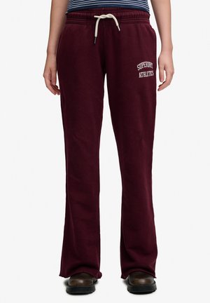 Maroon Superdry Athletics sweatpants med hvid snor, båret med sorte sko og stribet top, vist fra taljen til fødderne.